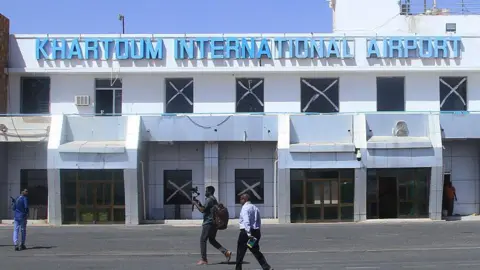 AFP via Getty Images A general view of the outside of Khartoum International Airport on 26 February 2026. Three people are walking in front of the airport