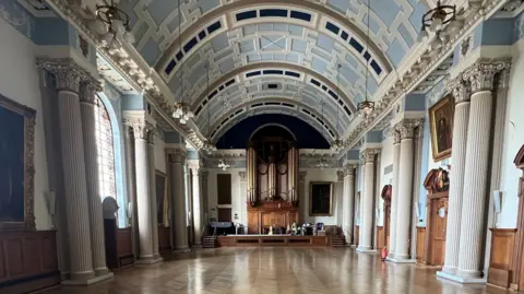 Colchester City Council A hall with very clean floor and high ceilings with designs on them.