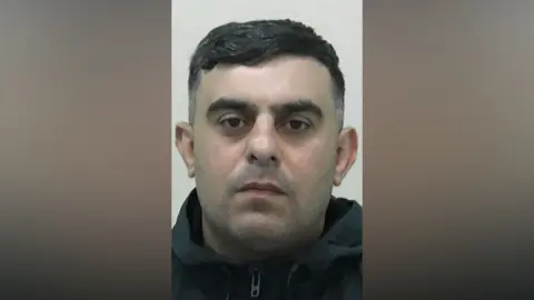 Mugshot of Murad Ibrahim. He has slight dark stubble and short black hair. He is wearing a black zipped hoodie.
