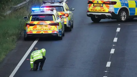 A police officer on a road alongside three police cars. 