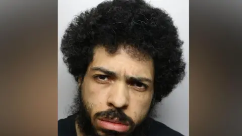 A police mugshot of Jason Spence, with curly black hair and a beard.