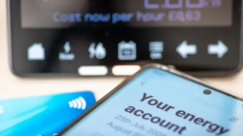 Getty Images Smartphone displaying an energy account next to a bank card and in front of a smart meter display.