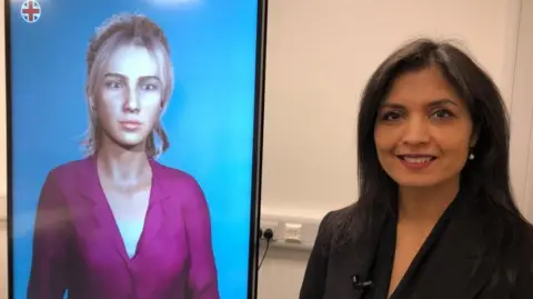 A woman is wearing a black suit, she has long dark hair she is standing next to a large screen with a female avatar on it wearing a purple shirt 