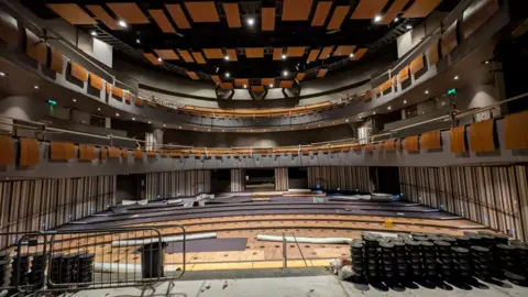 Shropshire Council Railings and other objects are in the foreground in the wide photo of the theatre. No seating is visible in the stalls and two other tiers are also in the image.