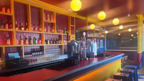 BBC The picture shows a bar with beer taps. The walls and bar top and red while the other colours in the room are yellow and blue
