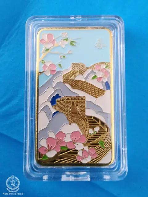 Polícia de Nova Gales do Sul Uma barra de ouro ilustrada com uma imagem colorida da Grande Muralha da China, em uma caixa de plástico com fundo azul.