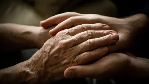 An older person's hands being held by a younger persons.