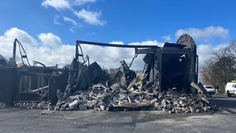 The picture shows one or more large sheds completely destroyed by fire