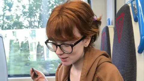 Clare Rogers A young woman on the train looking down at her lap