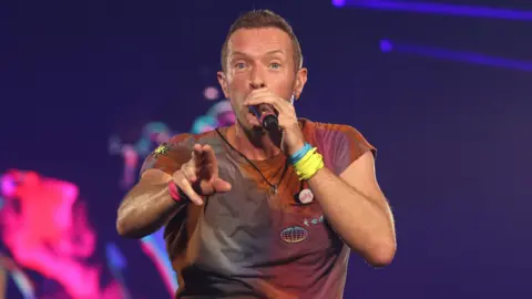 PA Media Chris Martin of Coldplay performs on stage