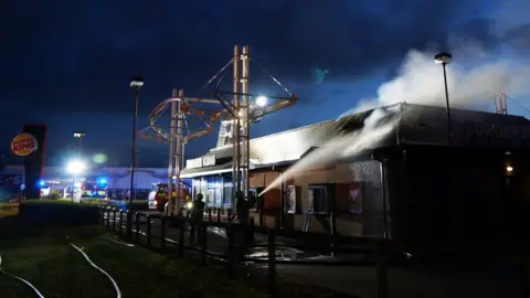 Bedfordshire Fire Service Fire crews tackle a fire at a Burger King in Bedford while smoke is seen coming from its roof.