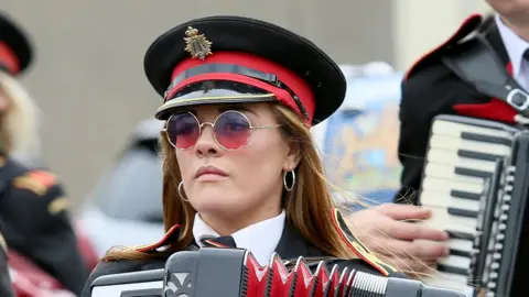 PAcemaker A woman wearing sunglasses and playing the accordion in uniform as part of Twelfth celebrations