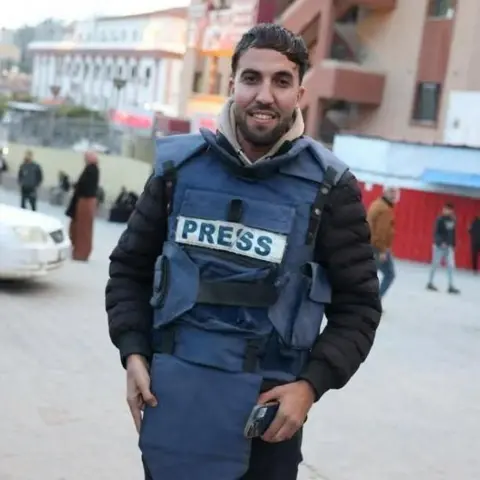 Reuters A man smiles at the camera wearing a press vest and holding a mobile phone in his hand