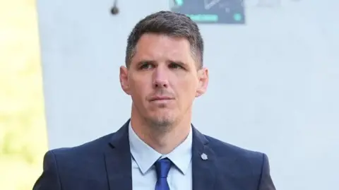 Paul Street wearing a navy suit jacket, navy tie and pale blue shirt as he arrives at a previous court hearing. He has short dark hair.