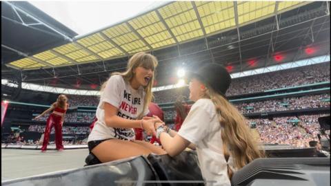 Talor Swift holds a young fan's hand after she gives them her hat