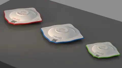 Design Innovation in Plastics Three CPR+Aid devices, designed by Harry Wragg, each a different size and colour on a dark grey table.