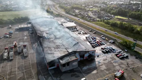 Richard Swingler Ron Skinner dealership building shown with considerable fire damage and smoke still rising