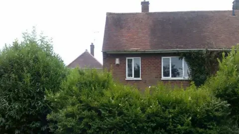 City of Wolverhampton Council The outside of one floor and the roof are visible. Bushes are covering other parts of the house in this image taken outside. Part of another property is visible in the background.