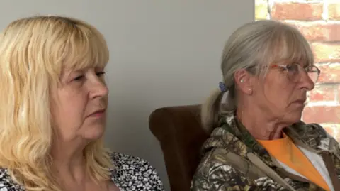 Karen is pictured on the left and has shoulder length blonde hair. Debbie is pictured on the right and has long grey/blonde hair tied in a pony tail. They are both listening to a conversation.