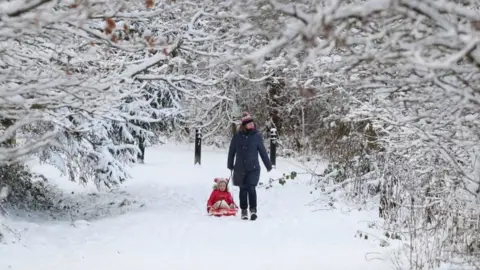 PA Media A woman tows a child on a sledge through a snow-covered wood at Larbert, near Falkirk in Scotland