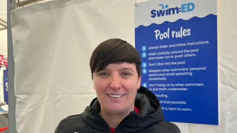 Tom Jackson/BBC Vicky, a woman with short hair, wearing a red T-shirt and a black hoodie, smiling for the camera.