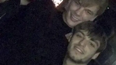 PA Media A blurry photo showing a smiling Lee Harrison, who has brown hair, posing with a taller man, Niall Barry, who has lighter blonde hair