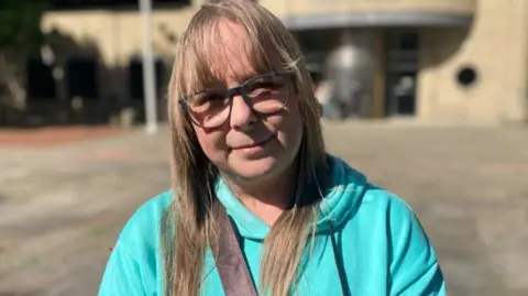 Emma Glasbey/BBC A woman in a turquise hoodie with a black bag strap across her, standing outside court, She has long blonde hair and glasses. 
