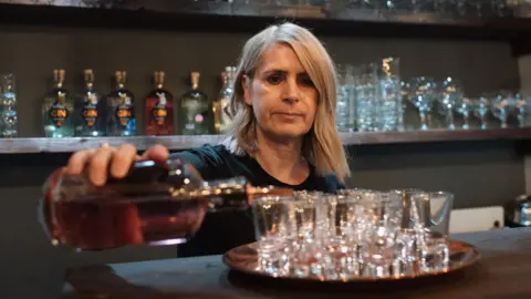 Woman working in bar pour alcohol into shot glasses