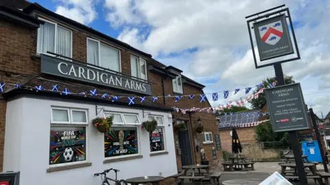 Kate Bradbrook/BBC The exterior of a pub that has Scottish flags and bunting put up all around it. Tables have been placed outside the pub. The windows have also been painted on in celebration of the FIFA World Cup.