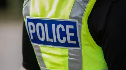 The back of a police officer's high-vis vest. It is yellow, with the word "Police" written across the back. 