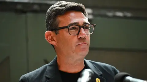 Getty Images Andy Burnham, who has dark hair, in front of a microphone. He is wearing a dark suit and t-shirt 
