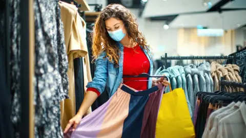 Getty Images A woman wearing a mask shopping for clothing