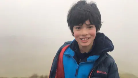 Gabriel out walking in a field with short dark hair in mist smiling at the camera.