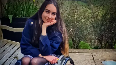 Bethany Handley Bethany Handley sitting in her wheelchair on a patio in front of some bushes