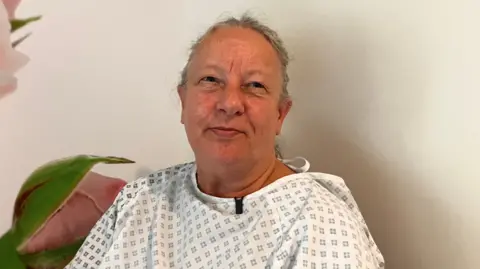 Vanda Instone in a hospital gown looking at the camera.