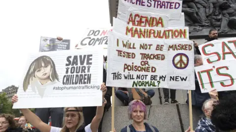 Getty Images QAnon slogans such as 'Save our children' were seen side-by-side with coronavirus conspiracy posters at Saturday's rally