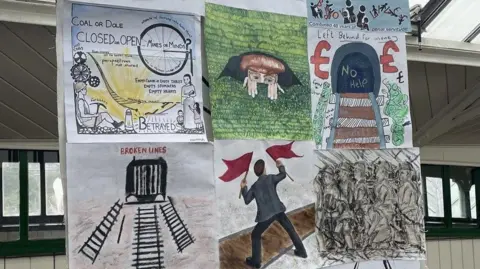 Amateur paintings and drawings which have been stuck to a banner, based on the events of the General Strike in the North East of England. Words and phrases adorn some of the artwork, such as "Coal or Dole" , "Left Behind for Money", and "Broken Lines". Most of the artwork depicts miners or railway immagery, in commemoration of the accidental derailing of a passenger train during the strike, which occured when striking miners sabotaged a local rail line to try and stop a coal train reaching its destination.