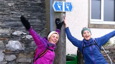 BBC Emma Blackburn and Maddie Landels next to a Raad Ny Foillan sign post