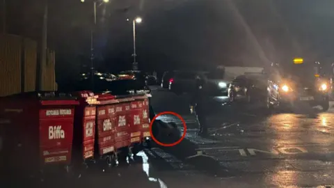 Supplied A dark image of a car park. A red circle outlines the blurred image of a man on the ground. One officer stands to the right.