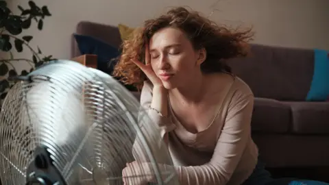 Woman with closed eyes sits in front of a fan as her hair is blown around