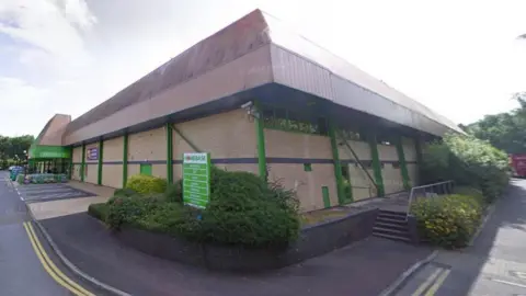 A view of the Homebase store at Rose Lane in Barnstaple. It is a brick building surrounded by shrubs 