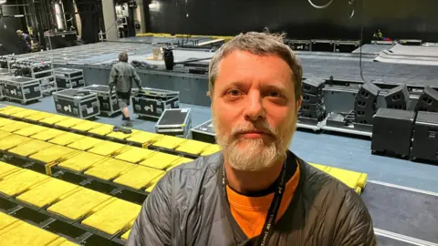 Photograph of Gary Briggs from Factory International. He is pictured in front of seats, inside the theatre, at the Aviva Studios in Manchester.