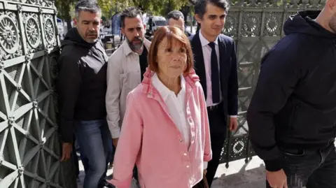 GUILLAUME HORCAJUELO/EPA/Shutterstock A woman in a pink top flanked by men enters court in the southern city of Nîmes 