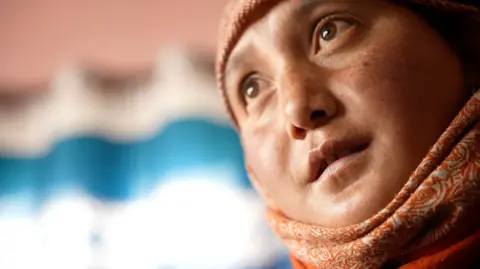 A woman wearing an orange scarf looks sideways