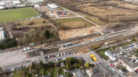 An aerial view of Eaglescliffe station. Cars can be seen parked outside of the station. Construction work can be seen taking place on the island platform. A large building site is present on the far side of the station.