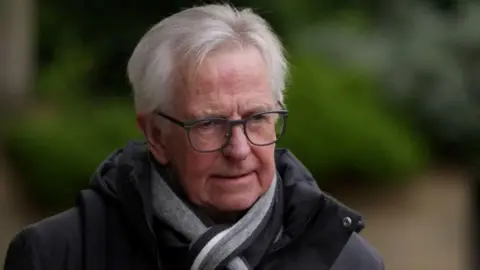 PA Media Lord Bracadale pictured in April 2024. He is wearing a grey jacket and scarf and has glasses.