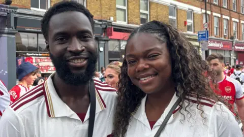 Close-up of Michael and Teju smiling into the cameras, both wearing white football jerseys.