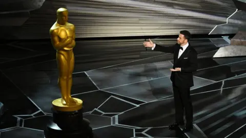 Getty Images Jimmy Kimmel stands next to a giant Oscars statue