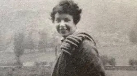 Green Family A vintage black and white photograph of Nan Green, smiling at the camera, with a large coiled rope over he shoulder