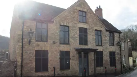 The Brockweir Inn Community Benefit Society A 16th Century brick building, formerly a pub. It is two storeys high and five large mullioned windows across. Old fashioned black metal wall-hung lamps are either side of the windows.
